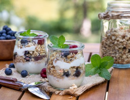 Photo for Yogurt parfait with granola, blueberries and raspberries garnished with mint outdoors on wooden patio table - Royalty Free Image