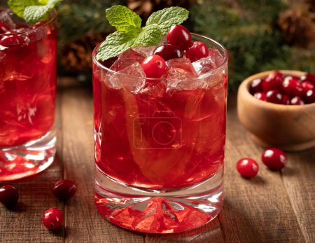 Photo for Cranberry cocktail with fresh cranberries and mint leaves on wooden surface. Fir tree branch and pine cones in background - Royalty Free Image