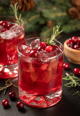 Photo for Cranberry cocktail with fresh cranberries and roseemary on black slate board. Fir tree branch and pine cones in background - Royalty Free Image
