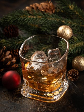 Foto de Vaso de whisky y hielo sobre superficie de madera con decoraciones navideñas de fondo - Imagen libre de derechos