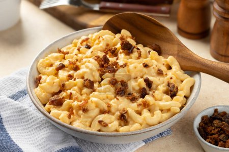 Téléchargez les photos : Macaronis et fromage avec morceaux de bacon dans un bol de service blanc et cuillère en bois - en image libre de droit