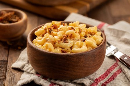 Photo for Macaroni and cheese with bacon pieces in a wooden bowl on a towl and rustic wooden table - Royalty Free Image