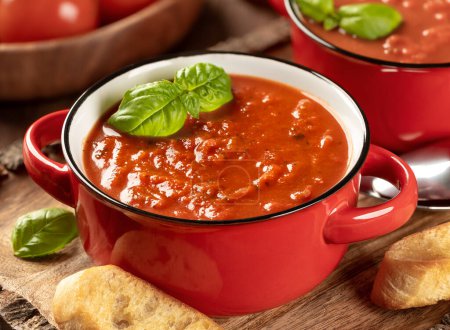 Téléchargez les photos : Bol de soupe aux tomates garni de feuilles de basilic et de tranches de baguette grillées sur un plateau en bois - en image libre de droit