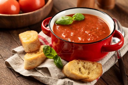 Téléchargez les photos : Bol de soupe aux tomates garni de feuilles de basilic et de tranches de baguette grillées sur un plateau en bois - en image libre de droit