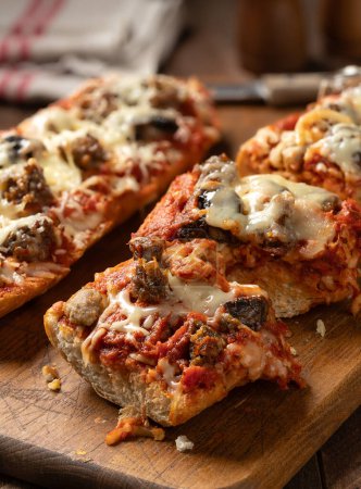 Foto de Pan de pizza hecho con salchichas, queso mozzarella y tomate en rodajas en una vieja tabla de cortar de madera - Imagen libre de derechos