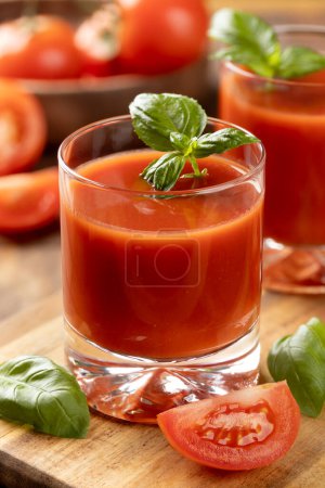 Foto de Dos vasos de jugo de tomate con hojas de albahaca y tomates en rodajas sobre una mesa de madera - Imagen libre de derechos