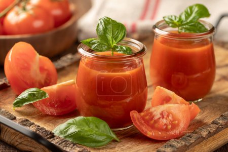Foto de Dos vasos de jugo de tomate con hojas de albahaca y tomates en rodajas en una bandeja de madera - Imagen libre de derechos