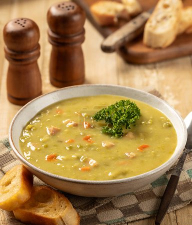 Téléchargez les photos : Bol de soupe de pois cassés au jambon et carottes garni de persil et baguette grillée sur une table en bois - en image libre de droit