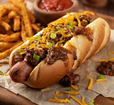 Photo for Chili hot dog with shredded cheddar cheese and seasoned french fries on a wooden board - Royalty Free Image