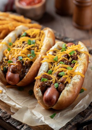 Téléchargez les photos : Deux hot-dogs au chili avec fromage cheddar râpé et oignons verts hachés sur un plateau en bois - en image libre de droit