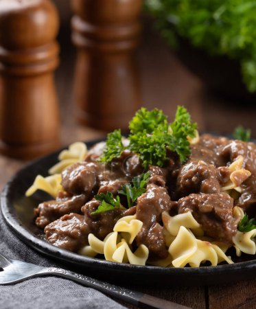 Photo for Beef stroganoff with egg noodles garnished with parsley on a black dinner plate - Royalty Free Image