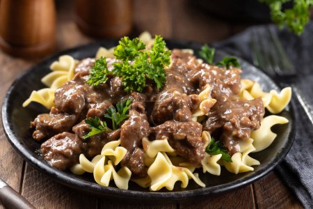 Photo for Beef stroganoff with egg noodles garnished with parsley on a black dinner plate - Royalty Free Image