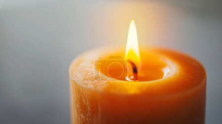 Close-up of a burning candle with a warm flame, soft glow on a blurred background.