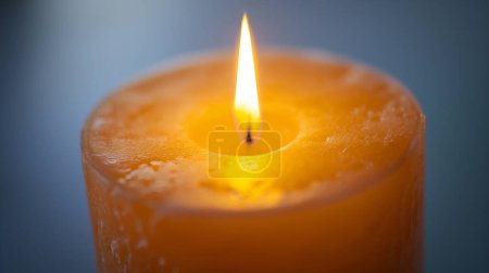 Nahaufnahme einer brennenden orangefarbenen Kerze mit schmelzender Wachsoberfläche und glühender Flamme.
