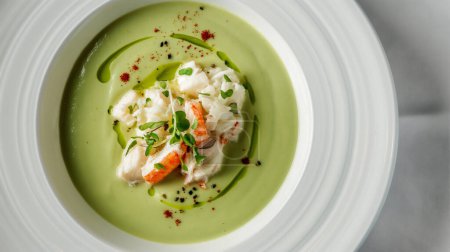Elegant presentation of crab meat in a vibrant green soup, garnished with herbs.