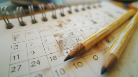 Worn pencils on a stained paper calendar, symbolizing heavy scheduling, planning.