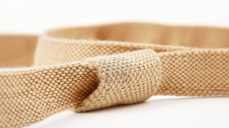 Cinturón tejido beige sobre una superficie blanca, detalle de textura y artesanía.
