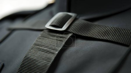 Close-up of a black strap with a metal buckle on a backpack, detailed texture focus.