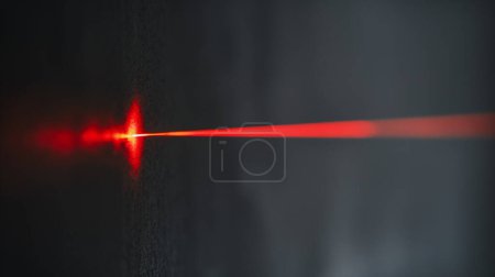 Rayo láser rojo con un punto focal brillante sobre un fondo oscuro.