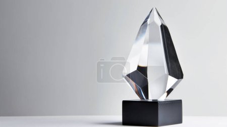 Téléchargez les photos : A crystal trophy with geometric facets on a black pedestal against a gray background. - en image libre de droit
