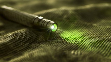 Laser pointer emitting a green beam on textured fabric surface.