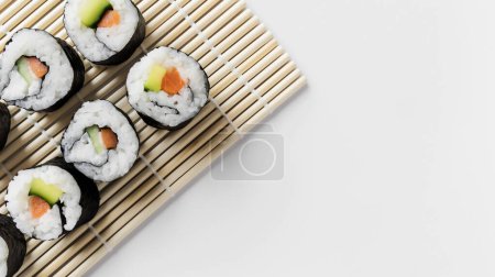 Téléchargez les photos : Rouleaux de sushi soigneusement placés sur un tapis de bambou, mettant en valeur la simplicité et l'élégance de la cuisine japonaise. - en image libre de droit