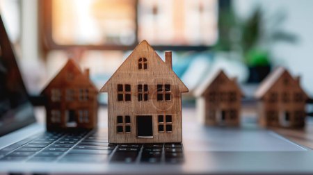 Petits modèles de maison en bois disposés sur un clavier d'ordinateur portable, symbolisant l'immobilier et la gestion immobilière en ligne.