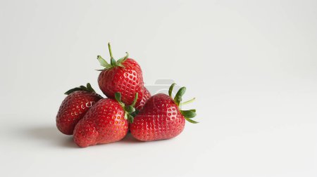 Fresh, ripe strawberries with green stems piled on a white background.