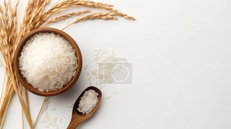 Cuenco de madera y cuchara llena de arroz blanco, rodeada de tallos de arroz sobre un fondo blanco, creando una escena simple y natural.