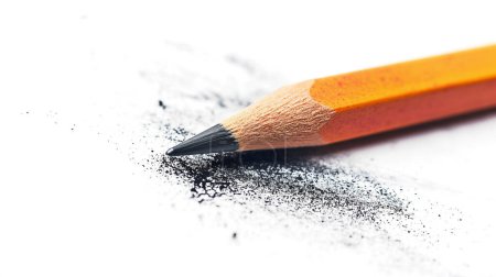 Close-up of a sharpened pencil with graphite shavings and dust scattered around on a white surface, highlighting creativity and writing.