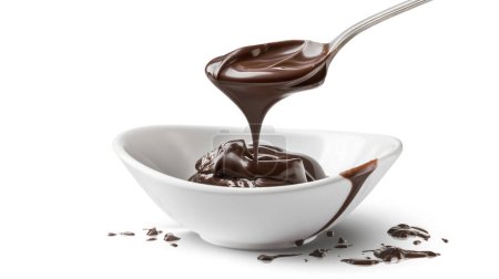 Smooth, rich chocolate sauce being poured from a spoon into a white bowl, with a few drips on the bowl's edge.