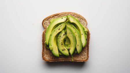 A slice of whole grain toast topped with neatly arranged avocado slices, seasoned with black pepper on a white background.