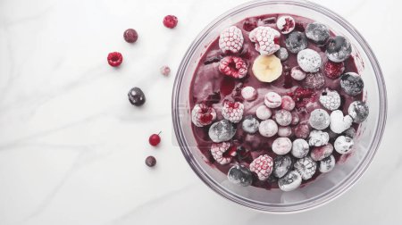 Bowl of frozen mixed berries and a banana slice on a marble surface, showcasing a refreshing and healthy dessert.