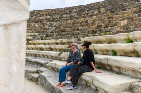 2 women sitting in an amphitheater in an ancient ruined city, reconstruction, restoration 10