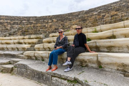 2 mujeres sentadas en un anfiteatro en una antigua ciudad en ruinas, reconstrucción, restauración