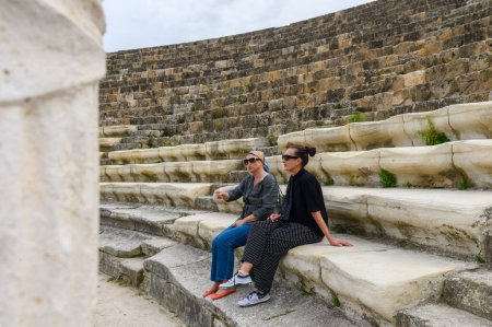 2 women sitting in an amphitheater in an ancient ruined city, reconstruction, restoration 12