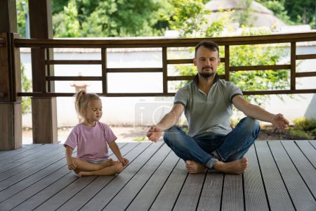 Foto de Padre e hija sentados en el suelo de madera, meditando con los ojos cerrados, actividad familiar al aire libre, paz y salud. - Imagen libre de derechos