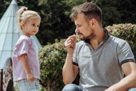 Kleines kaukasisches vierjähriges Mädchen, das seinem Vater am Vatertag eine kleine Blume schenkt. Vater riecht die Blume. Sommerzeit.