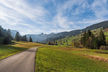 Foto de Camino en el paisaje montañoso en la región de Toggenburg con casas rurales, prados verdes y pastos, Mt. Speer en el fondo, Nesslau, Canton St. Gallen, Suiza - Imagen libre de derechos