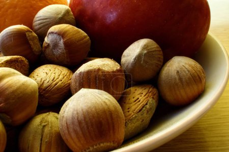Photo for Raw almond, hazelnut in the plate with an apple in the background high contrast - Royalty Free Image