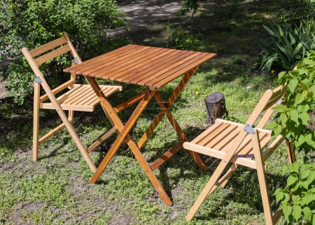 Photo for Empty chairs and table table in orchard. Set of folding wooden garden furniture - table and chairs on the lawn. Family Home Backyard Party Or Picnic Conceptual Scene. Teak wood garden furniture set - Royalty Free Image