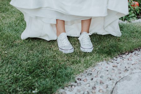 Foto de Pies de novia con zapatillas blancas y vestido de novia en hierba verde - Imagen libre de derechos