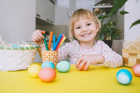 Foto de Smiling little girl with colorful eggs preparing for Easter Holiday. Kids painting easter eggs. Creative background for preschool and kindergarten. Family traditions and symbols of celebration. - Imagen libre de derechos
