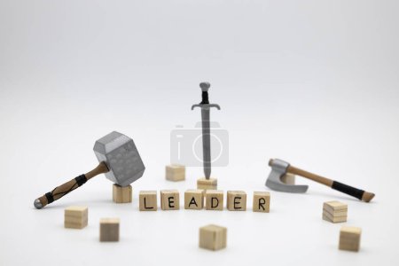Photo for The wooden cubes with the word LEADER and the weapon around against white background. The medieval weapons is hammer, sword and axe. - Royalty Free Image