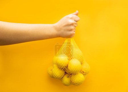 Photo for Lemons on a yellow background. Close-up hand holding a bunch of lemons. - Royalty Free Image