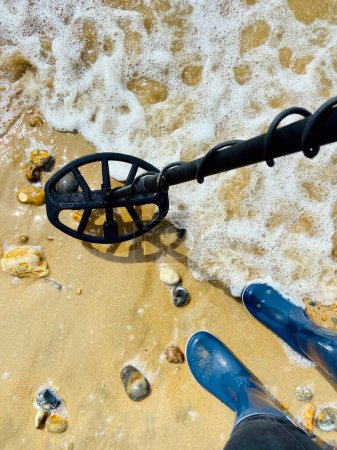 Foto de Detección de metales de playa con detector de metales negro océano detrás con botas de goma wellie - Imagen libre de derechos