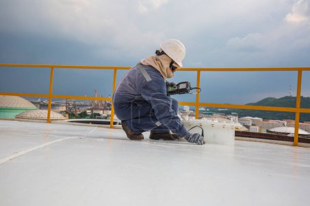 Téléchargez les photos : Travailleur masculin sont pour l'inspection à ultrasons épaisseur plaque de toit dessus du réservoir de stockage - en image libre de droit