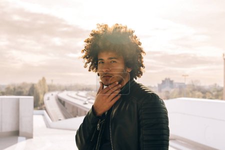 Téléchargez les photos : Fierté jeune afro-américain cool portrait d'homme à la mode avec les cheveux bouclés - lumière du jour chaude à l'extérieur en ville - en image libre de droit