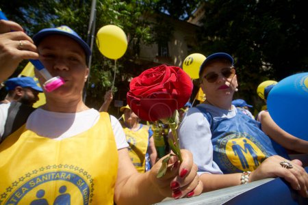 Téléchargez les photos : Bucarest, Roumanie. 8 juin 2023 : Une femme tenant une belle rose rouge sonne à la trompette lors de la manifestation des travailleurs de la santé devant le siège du ministère du Travail, à Bucarest. Jusqu'à quatre mille travailleurs de la santé syndicaliste de Roumanie "Sanit - en image libre de droit