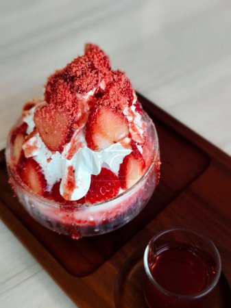 Erdbeer-Bingsu in einer Glasschale auf einem Holztablett. Farbenfrohes, köstliches Fruchteis mit Sirup ist servierfertig.